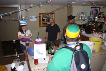 Minicon 42 bar, the bar itself, with three people behind the bar and one person in front.  Lights dangle about.